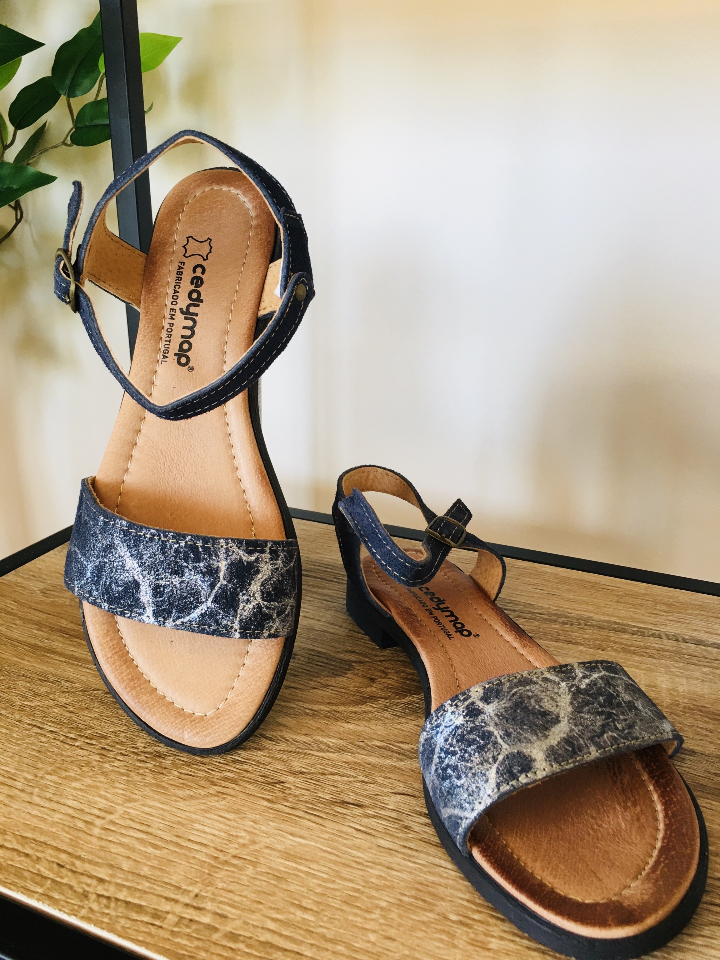 Sandálias femininas cedynap em padrão marmoreado cinza e marrom com tiras pretas e fivela, em superfície de madeira clara