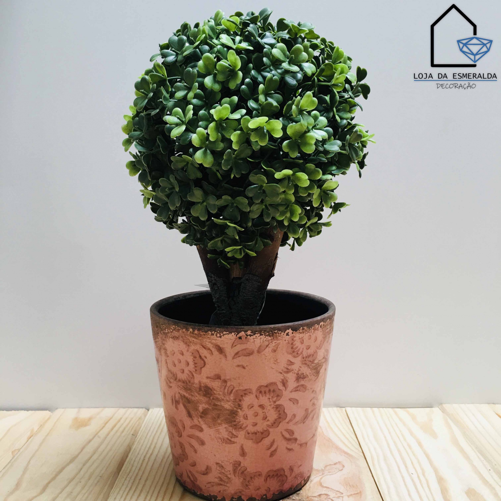 Planta artificial em vaso decorativo castanho com padrão floral sobre superfície de madeira clara