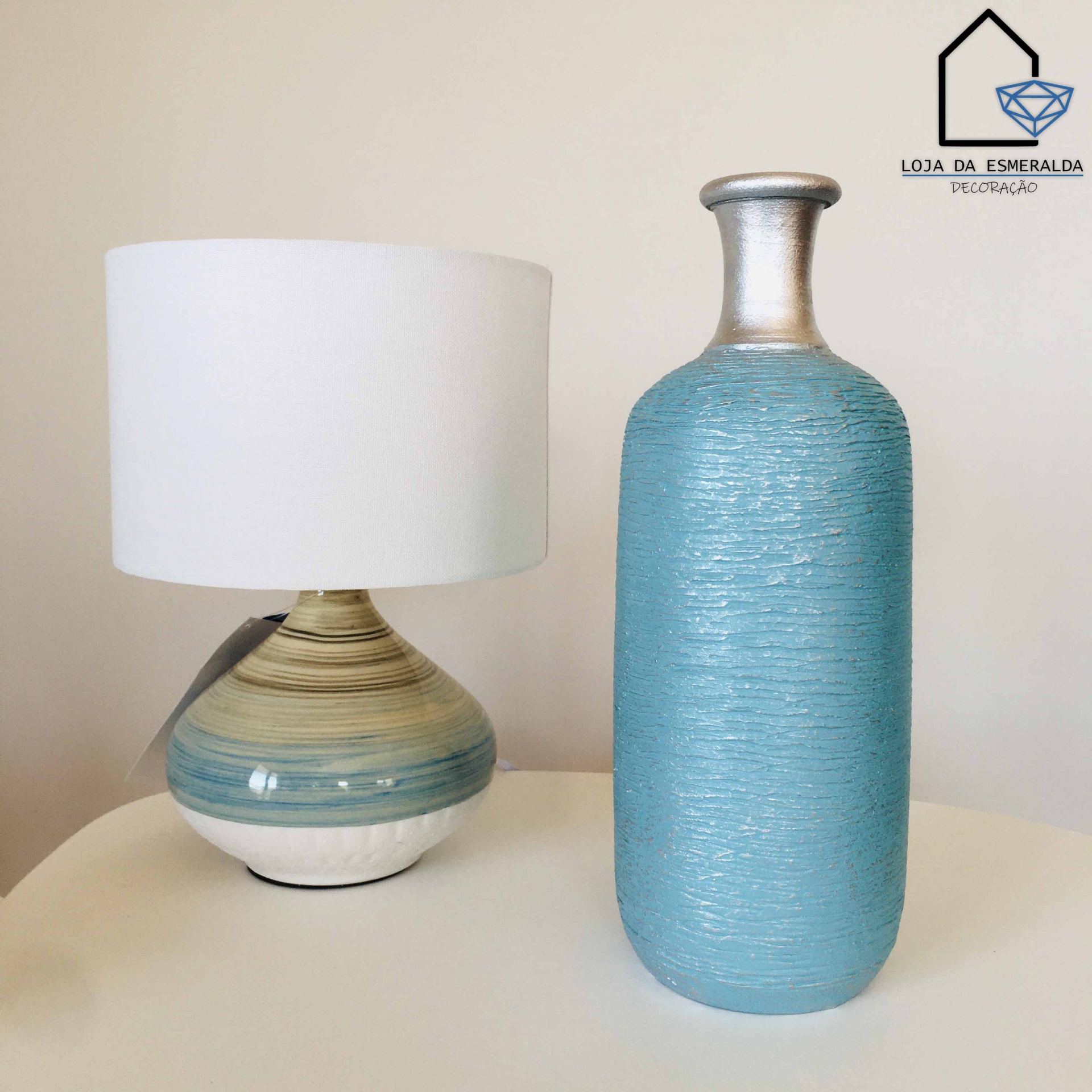 Candeeiro em cerâmica azul, bege e branco com cúpula branca e vaso texturizado azul turquesa com topo prateado sobre superfície branca