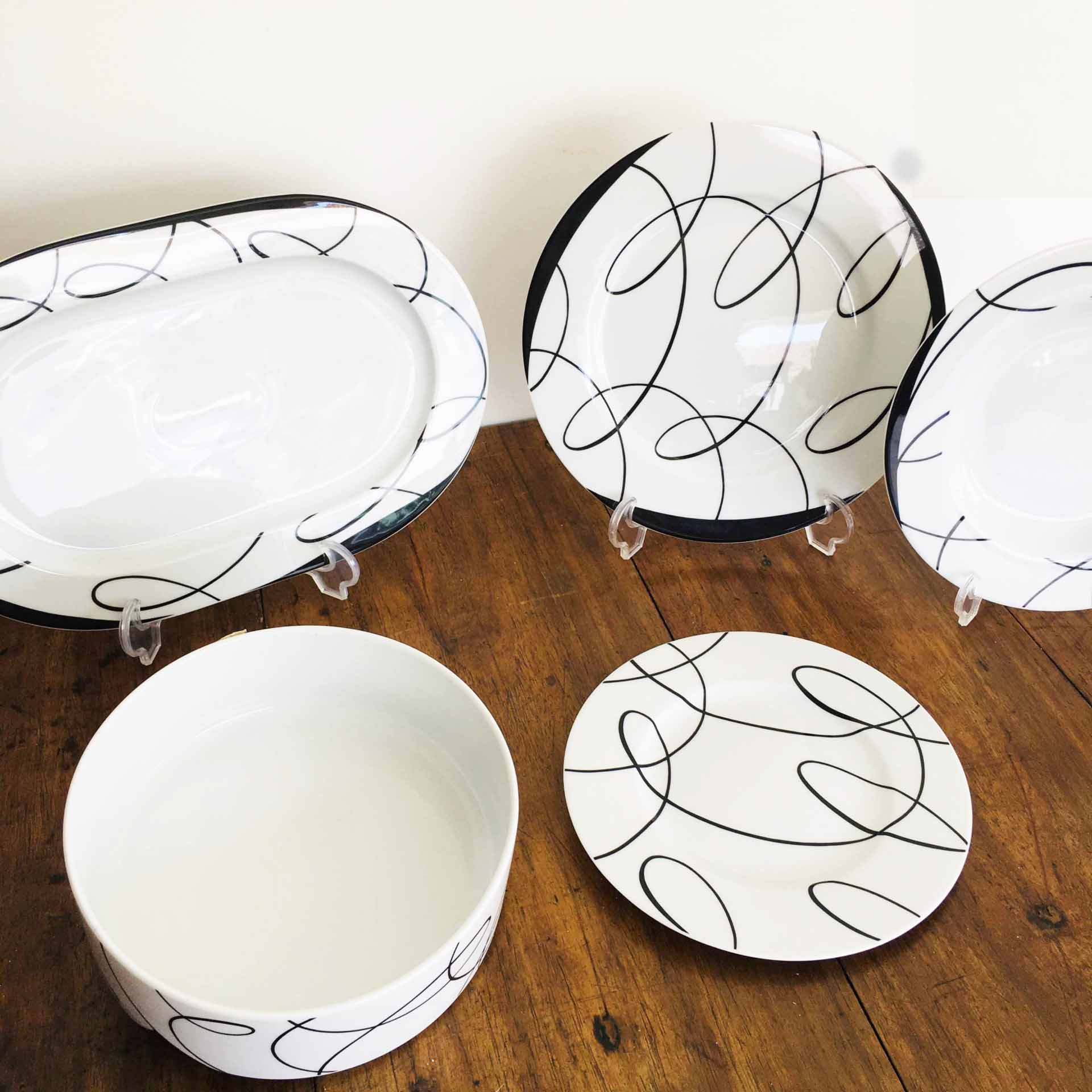 Conjunto de loiça branca com decorações pretas, sobre mesa de madeira.