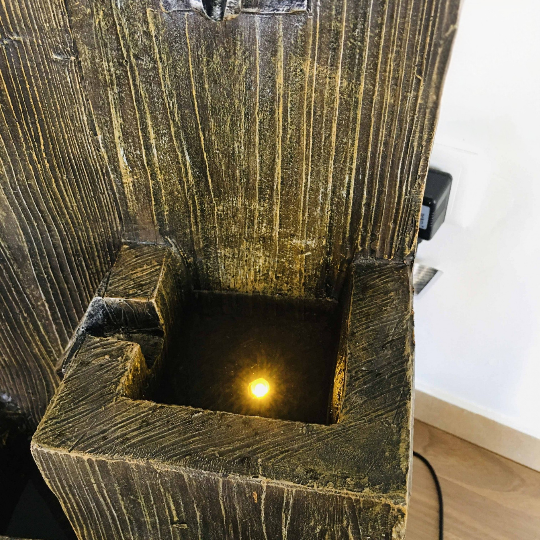 Fonte decorativa em madeira escura com água e luz refletida no interior
