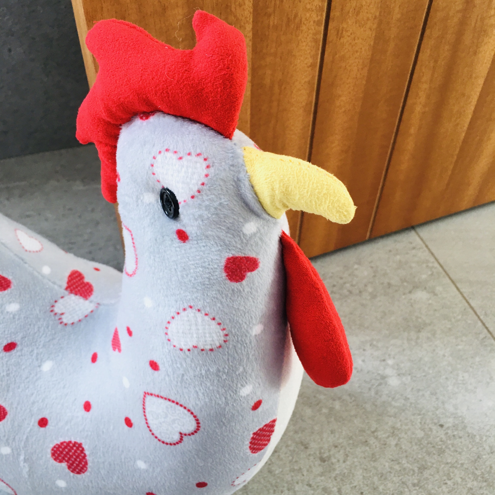 Pelúcia em forma de galinha com padrão de corações em fundo cinzento
