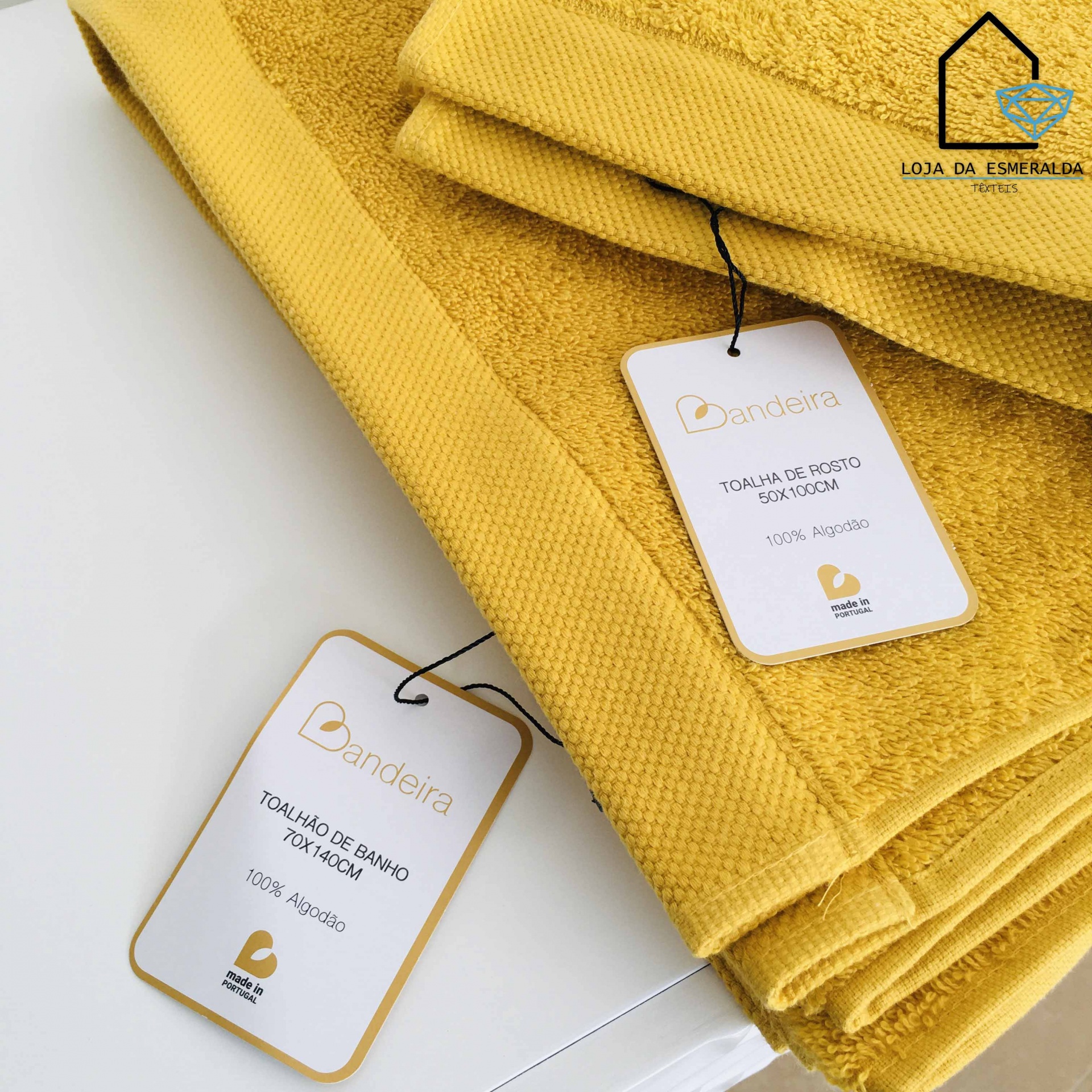 Conjunto de toalhas amarelas de algodão com etiquetas da marca Bandeira em superfície branca