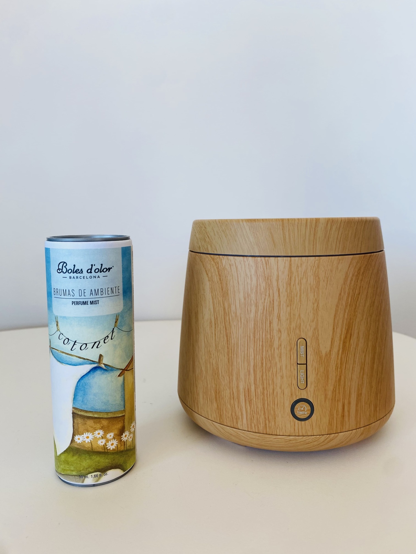 Difusor de ambiente em madeira clara ao lado de frasco cilíndrico de aroma com texto visível