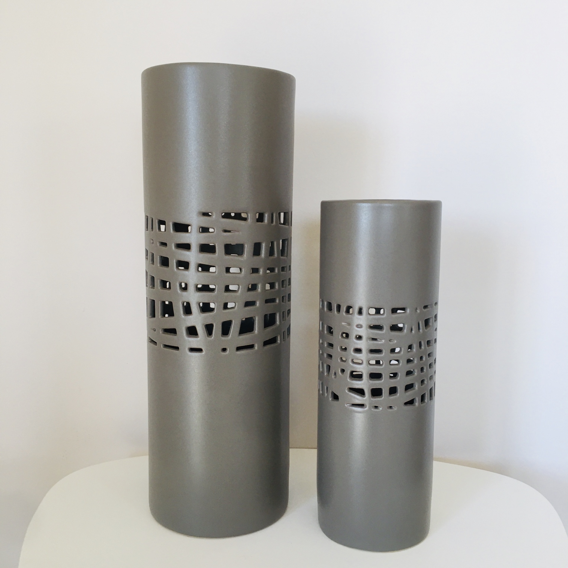 Dois vasos cilíndricos metálicos cinza com padrão recortado geométrico