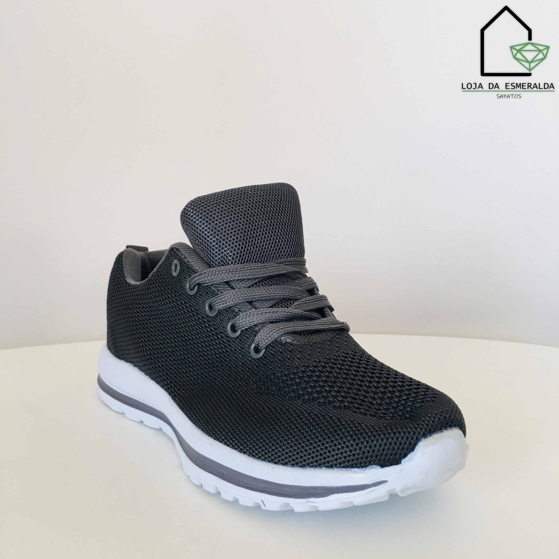 Ténis desportivo preto em malha com sola branca exibido sobre superfície branca