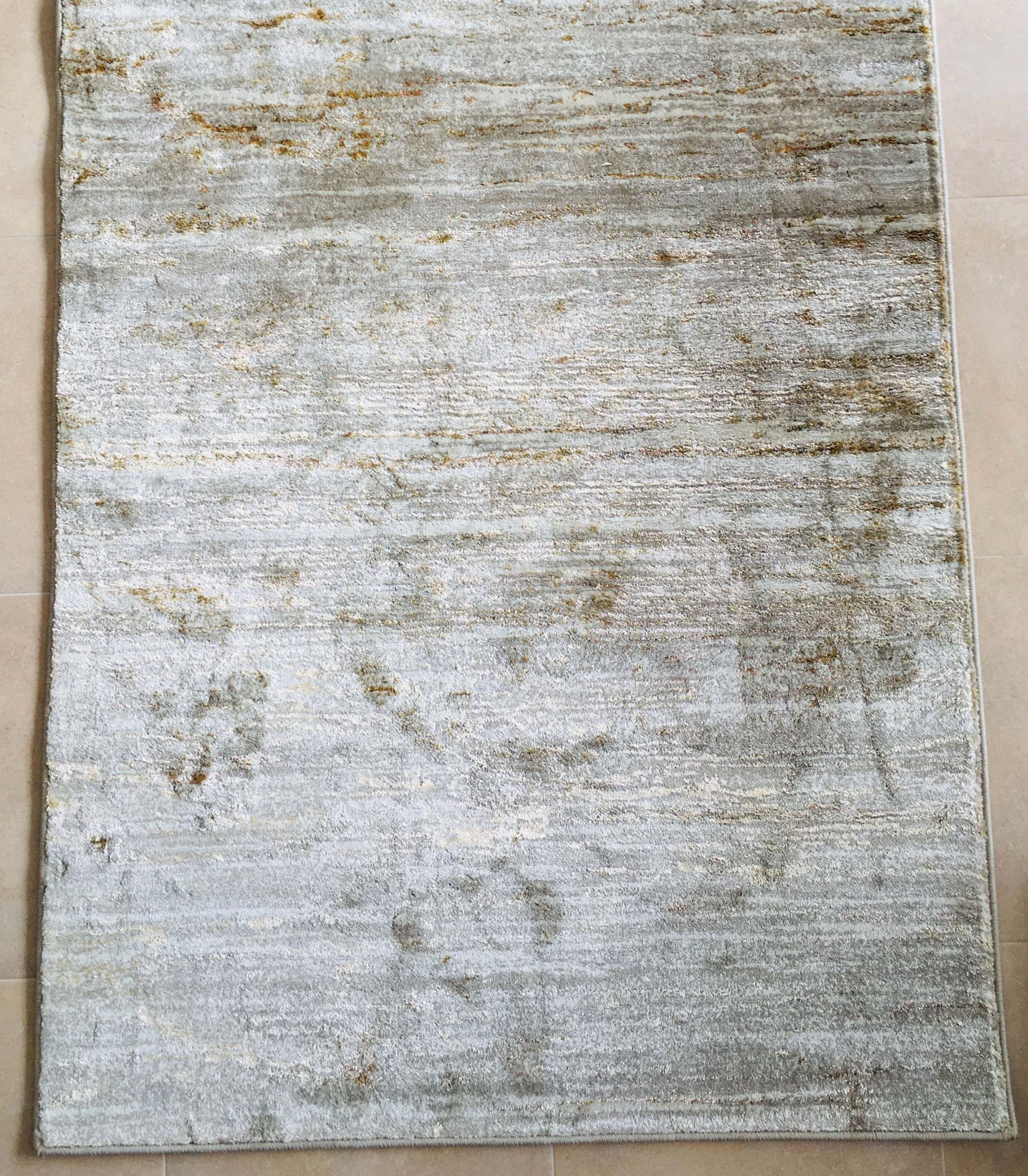 Tapete rectangular cinza claro e acastanhado sobre azulejos bege