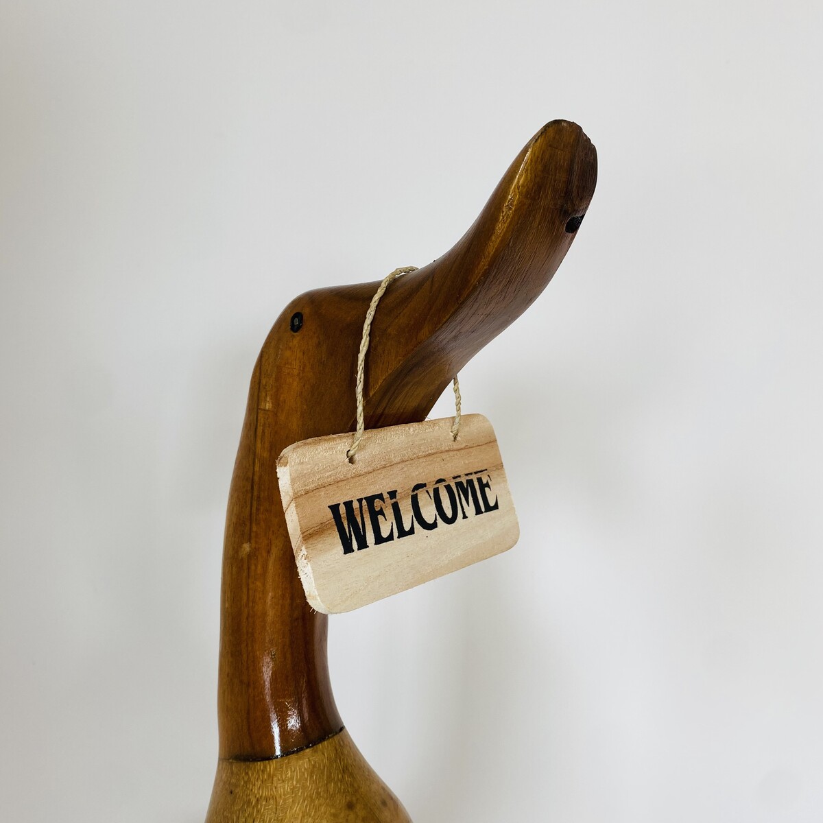 Figura de pato de madeira polida com placa 'WELCOME' pendurada no pescoço.