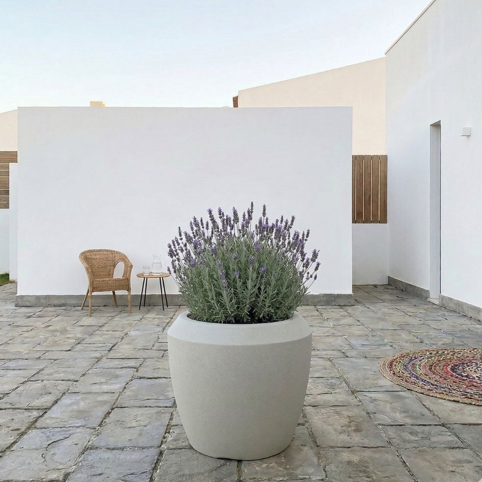 Vaso cinzento com lavanda num pátio de pedra com cadeira de verga e parede branca