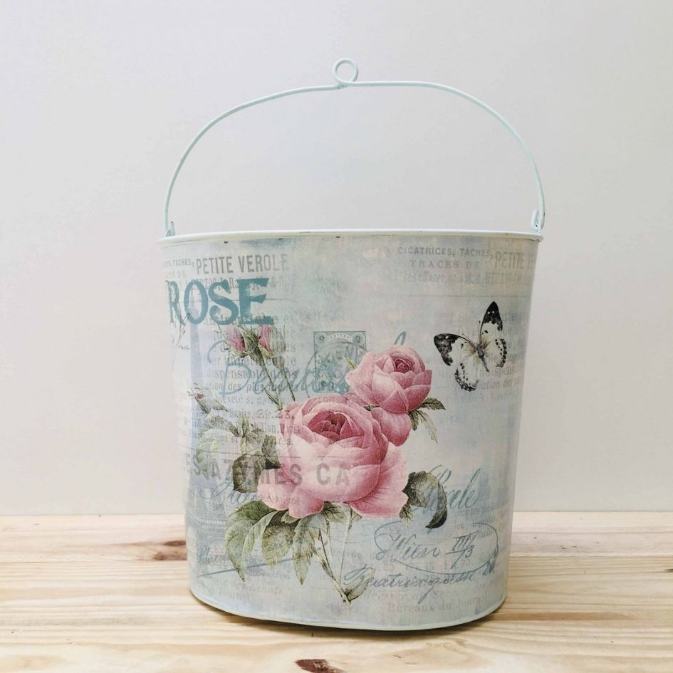 Balde metal decorativo com rosas e borboleta sobre madeira