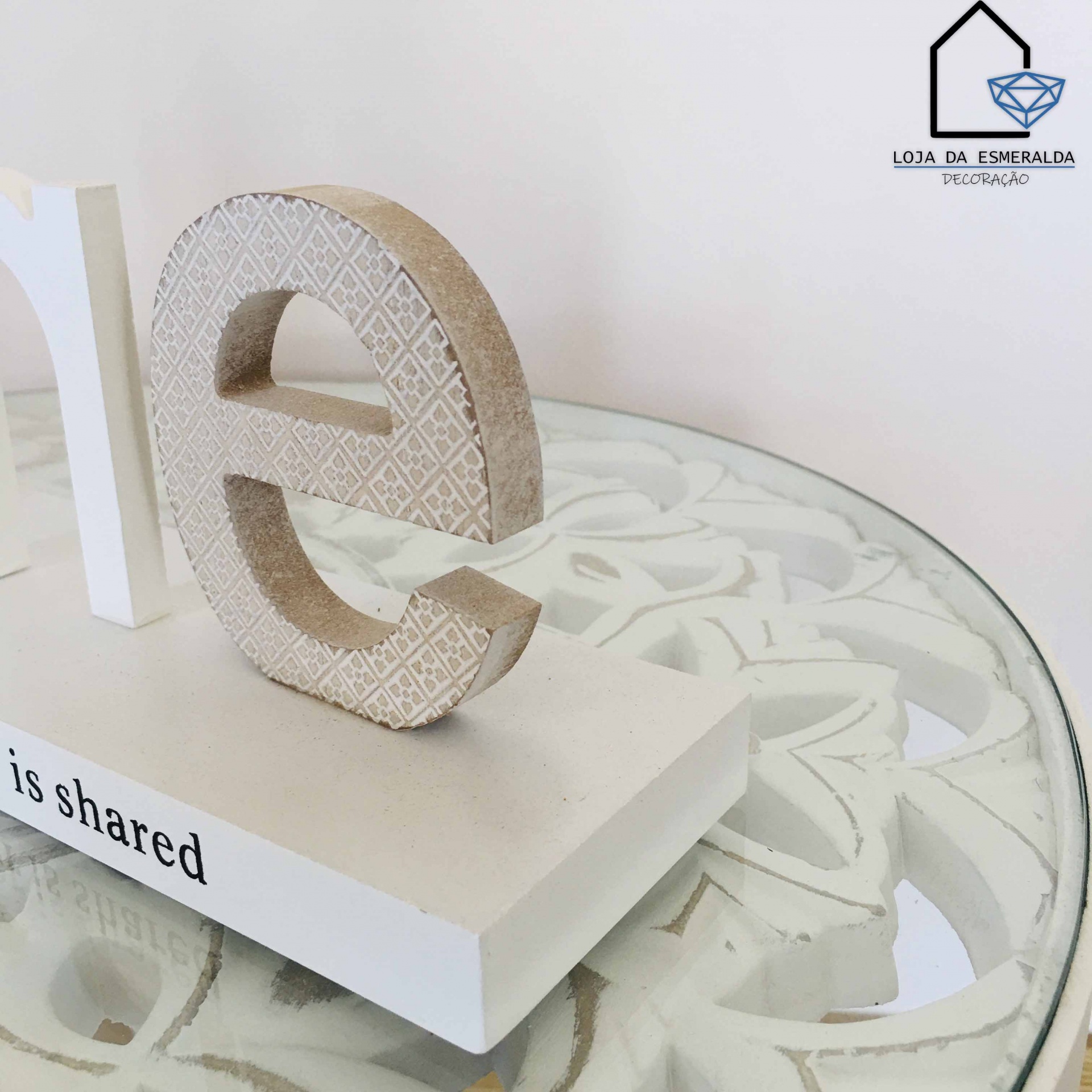 Objeto decorativo letra e bege com padrão geométrico numa base branca sobre mesa de vidro com design floral