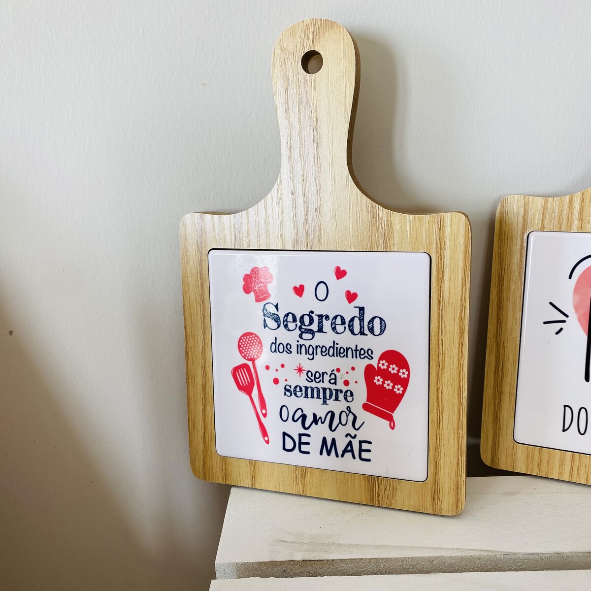 Tábua de madeira com azulejo decorativo com texto em português e desenhos de utensílios de cozinha.