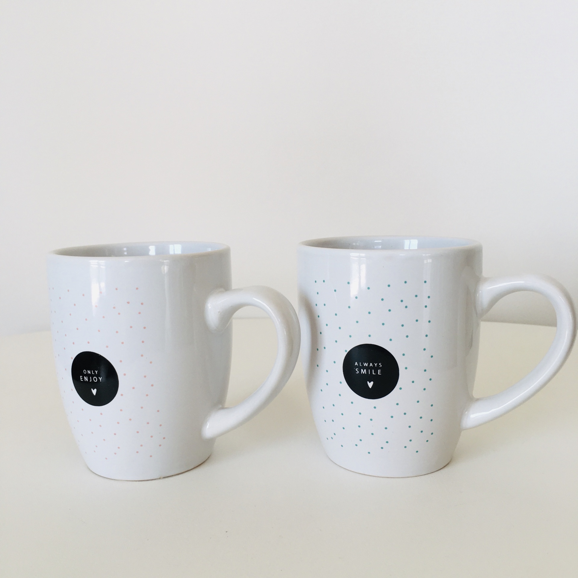 Duas canecas brancas com padrões de pontos e etiquetas pretas com texto