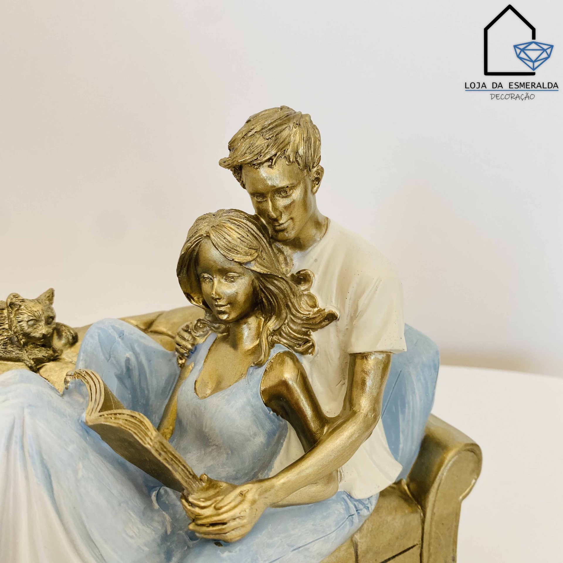 Escultura de casal no sofá com gato e livro, em tons bronze e azul claro