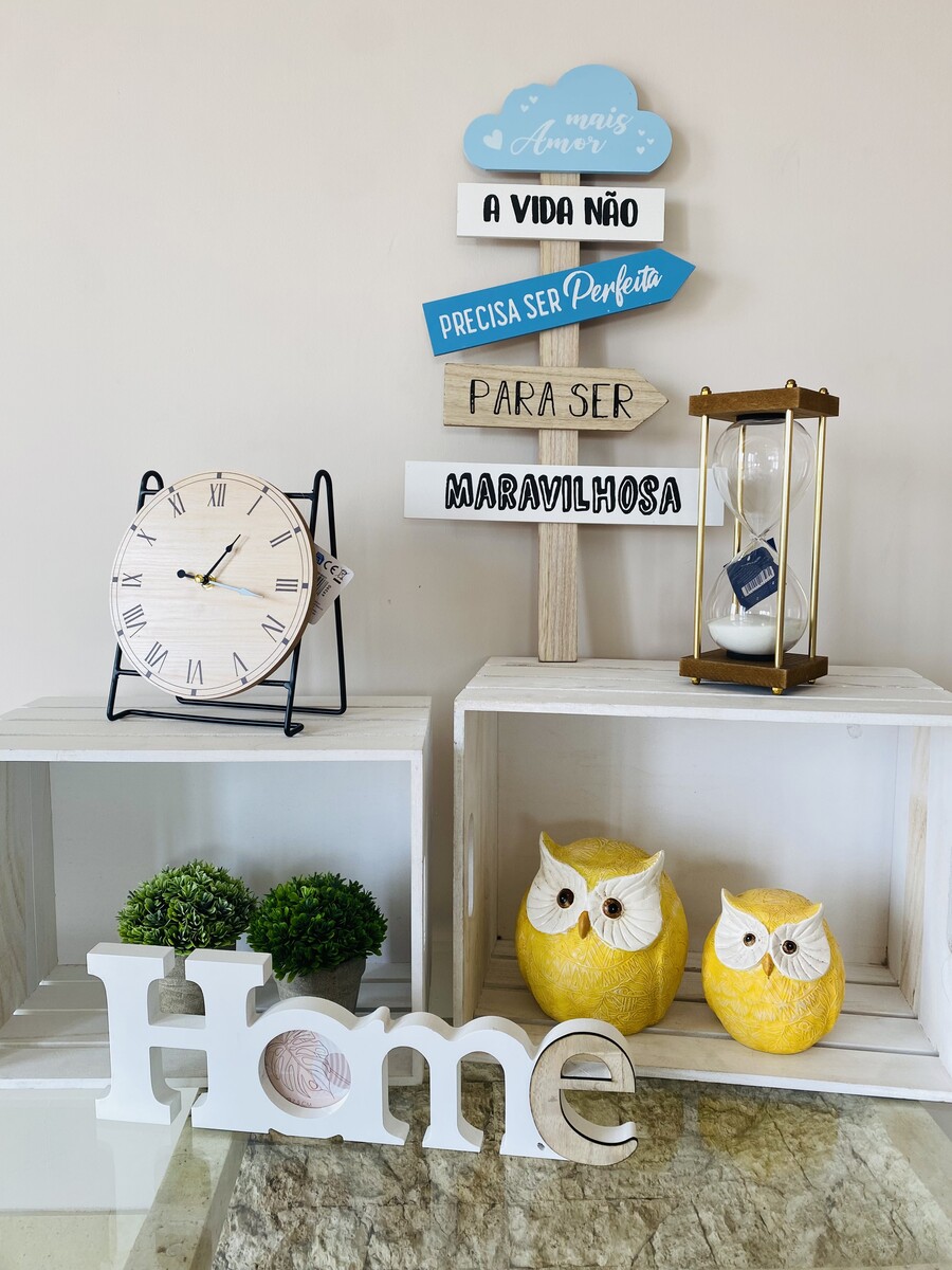 Relógio de mesa, esculturas de coruja, plantas, decoração com palavra HOME e placas de madeira com texto em português