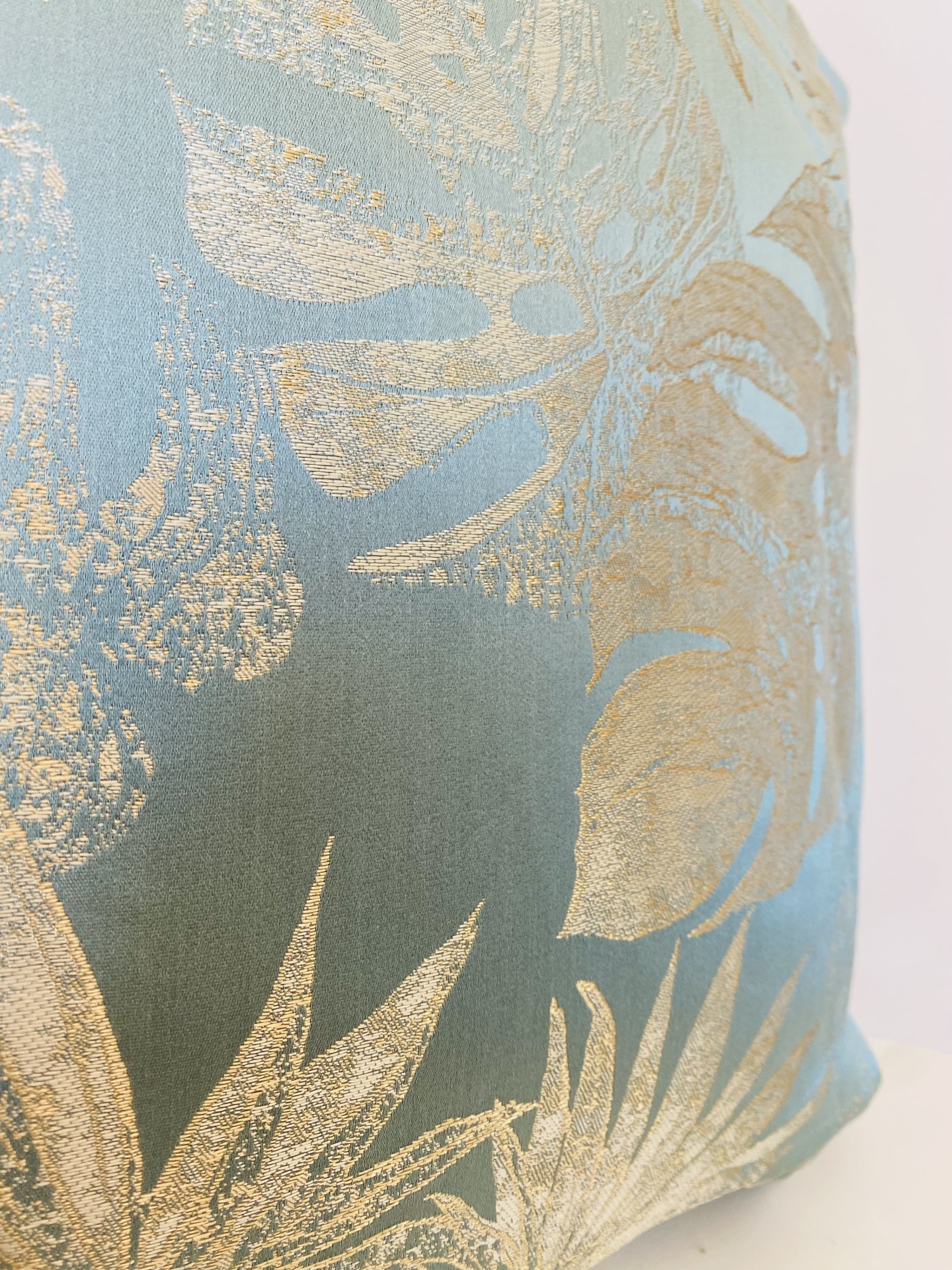 Almofada azul com padrão dourado de folhas tropicais bordadas