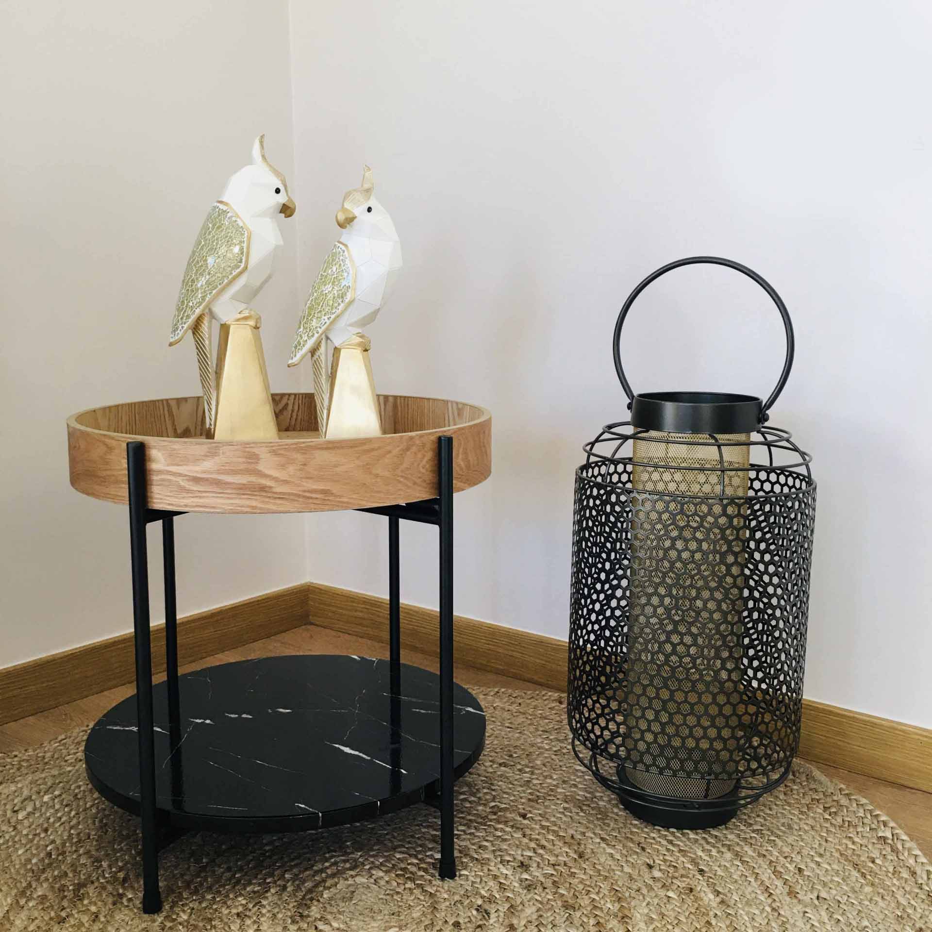 Mesa auxiliar com tampo de madeira e mármore, decorada com duas aves douradas e candeeiro metálico preto.