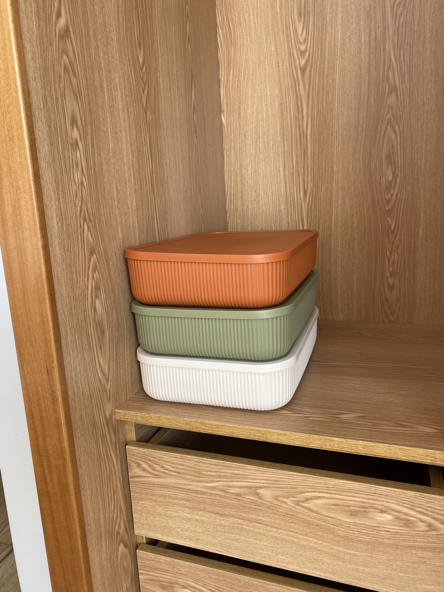 Caixas retangulares de plástico em três cores empilhadas numa prateleira de madeira.