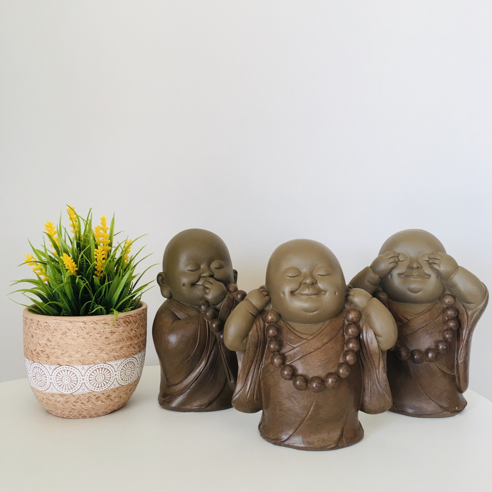 Três estátuas de monge budista castanhas com colares de contas e vaso de cortiça com planta amarela