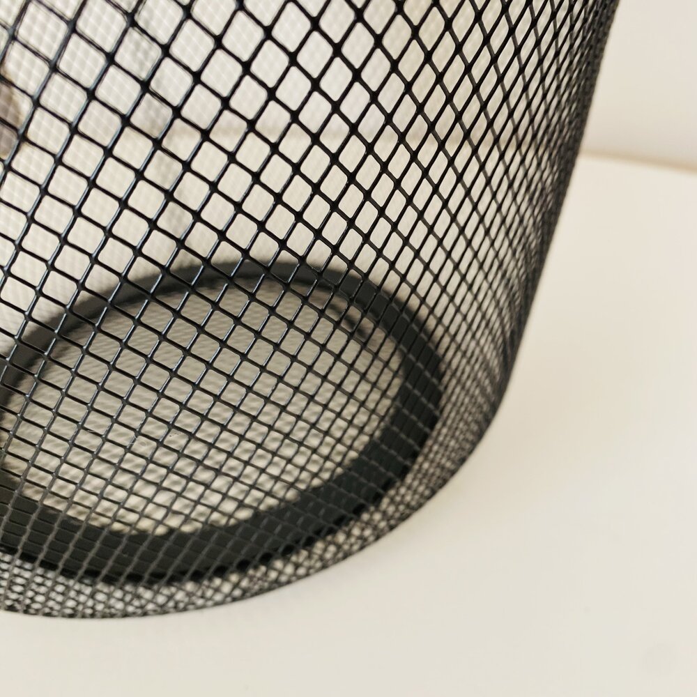 Cesto de metal preto em malha sobre superfície branca