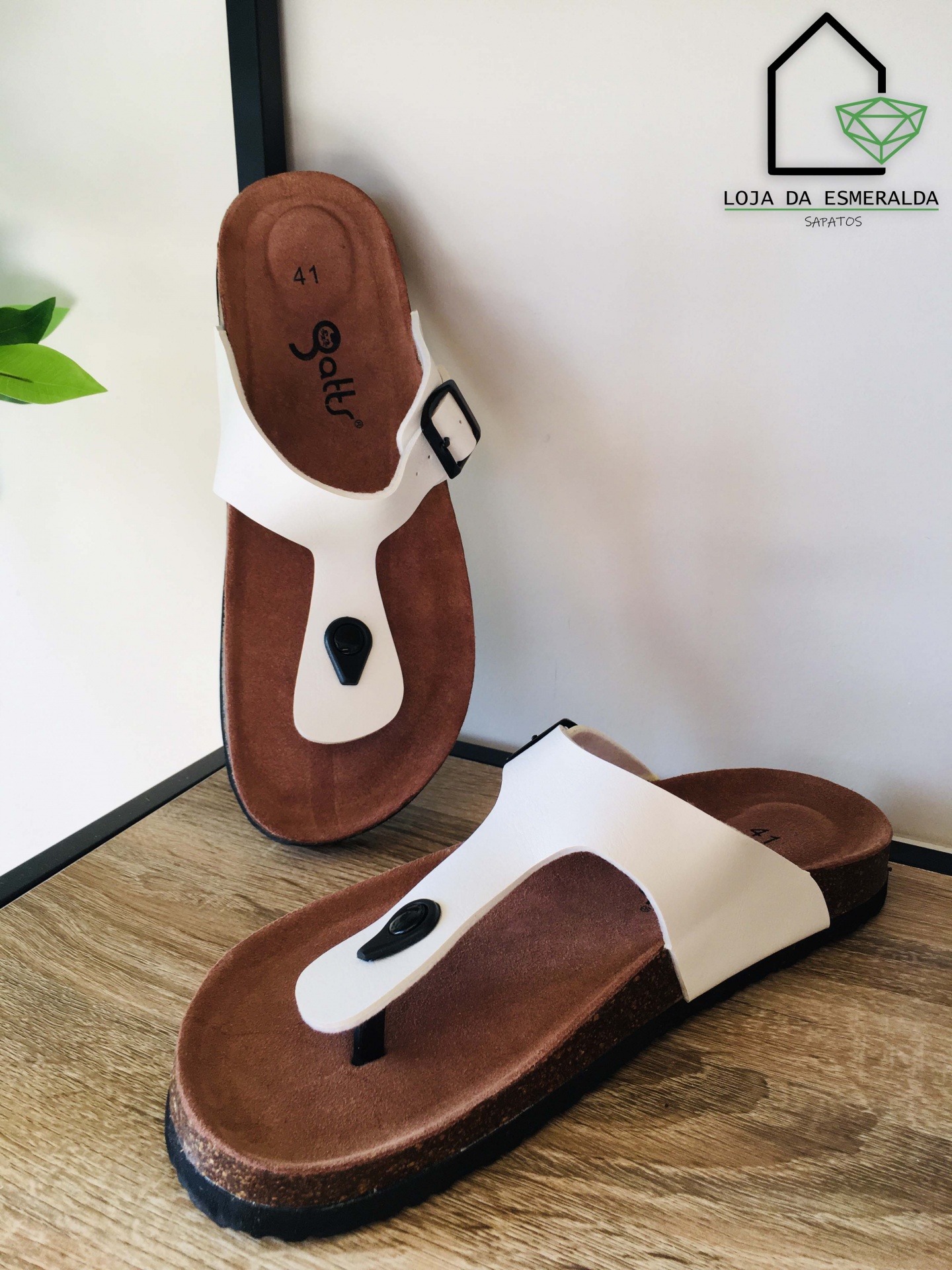 Sandálias brancas de dedo com sola castanha sobre superfície de madeira