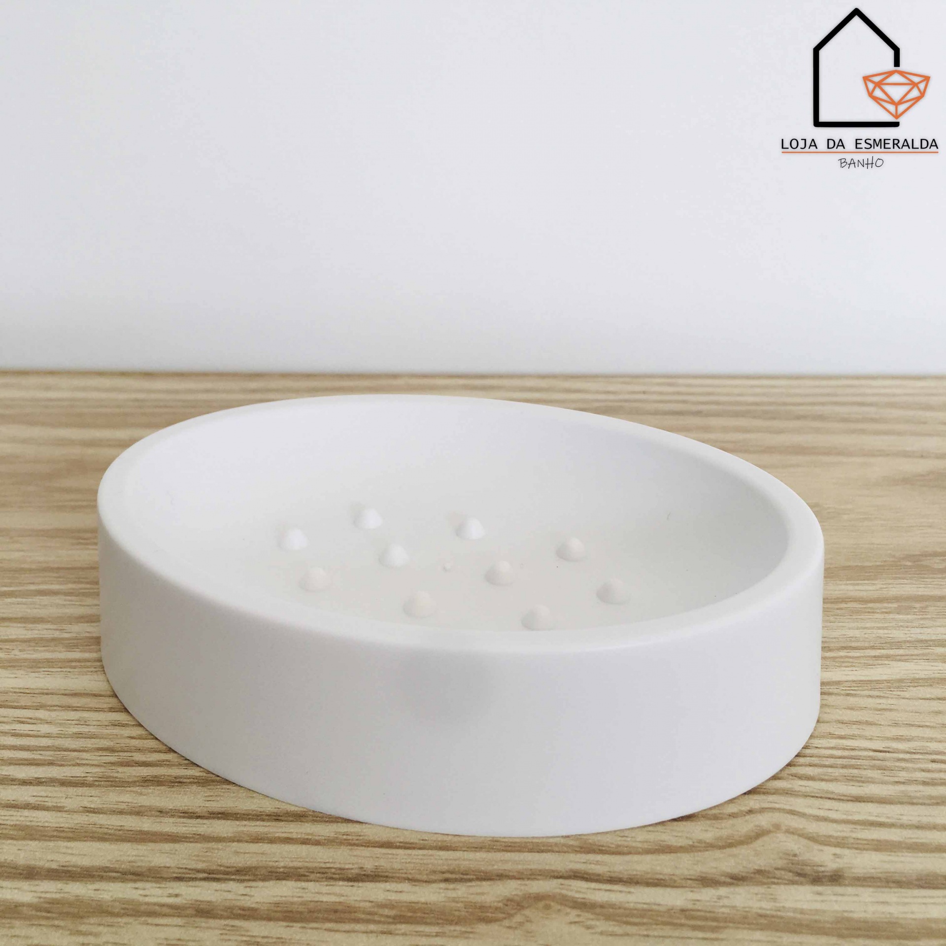 Saboneteira redonda branca em cerâmica sobre superfície de madeira com logotipo no canto superior direito