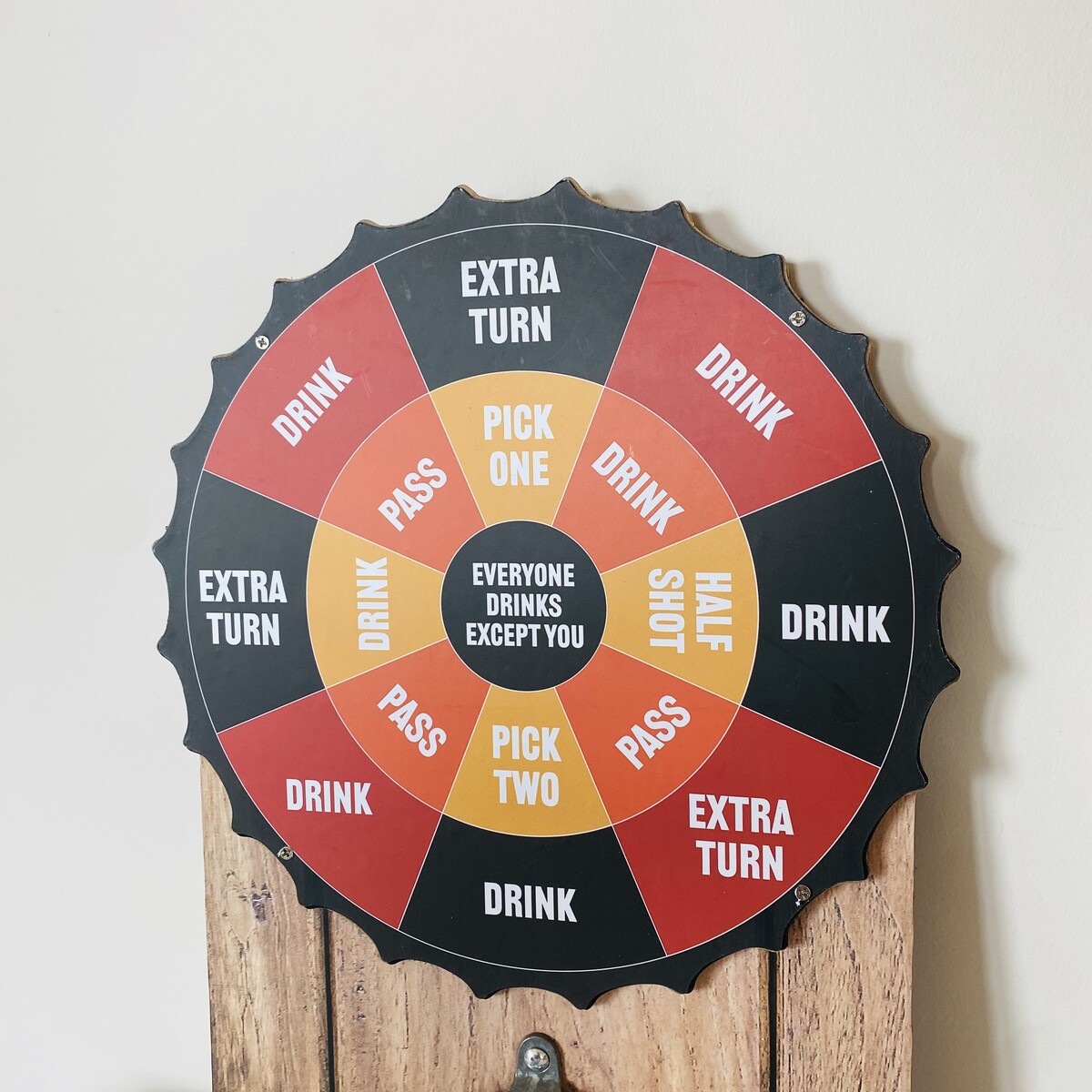 Disco tipo tampa de garrafa colorido com frases para jogo de bebidas montado numa superfície de madeira.