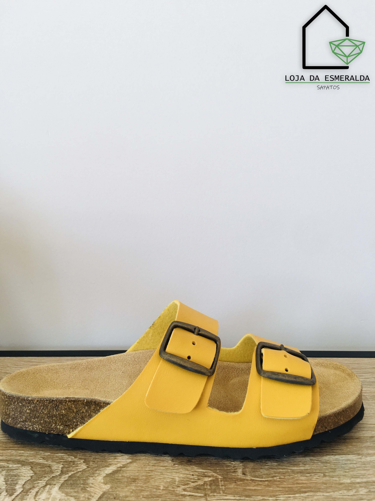 Sandália amarela com fivelas pretas e sola preta sobre madeira clara