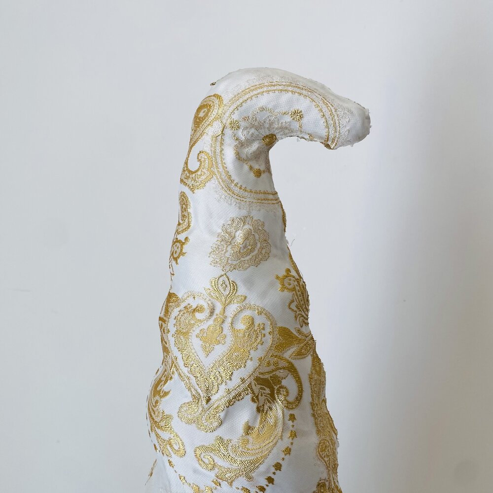 Pelúcia branca e dourada com padrão ornamental em fundo neutro.