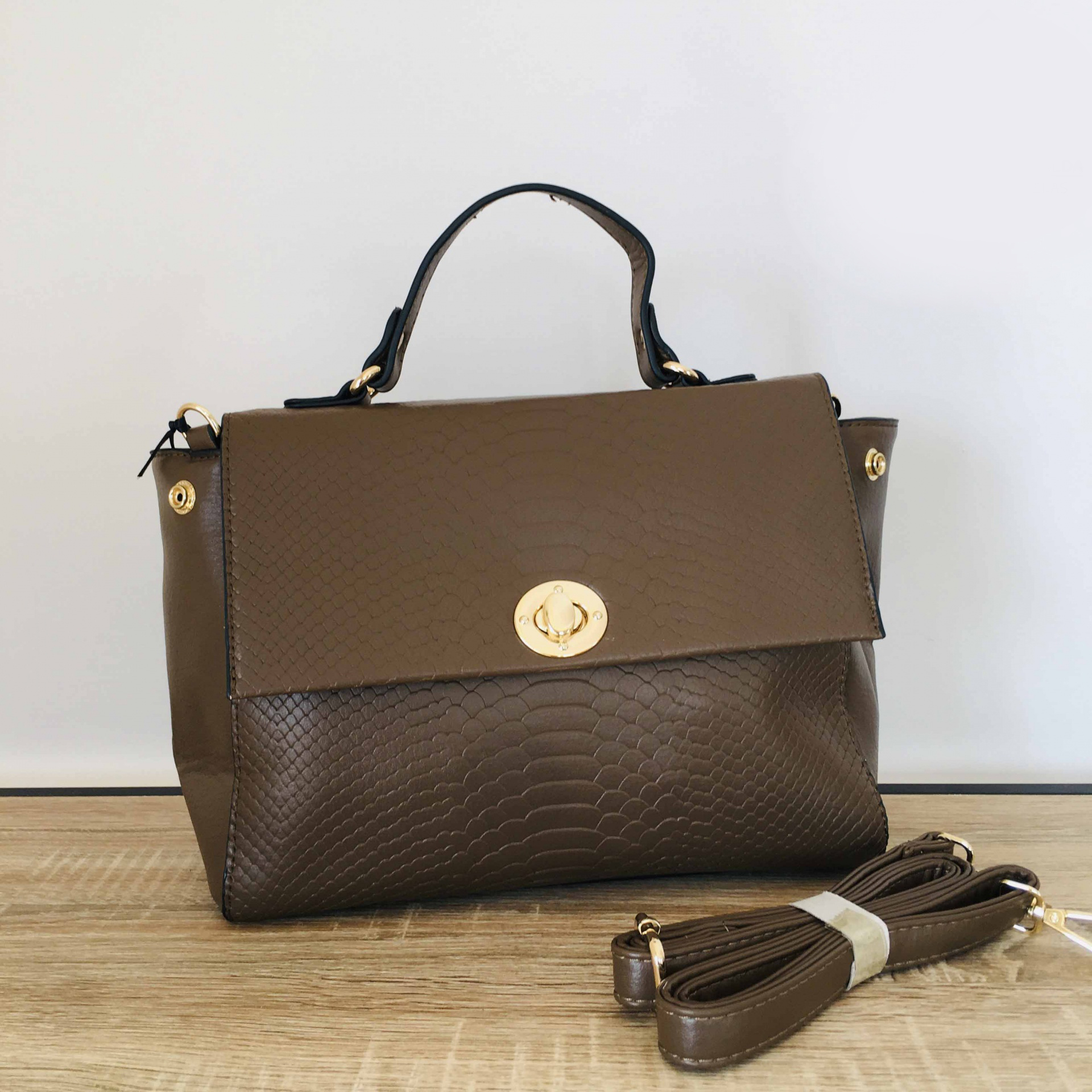 Mala castanha com textura de pele e fecho dourado sobre mesa clara