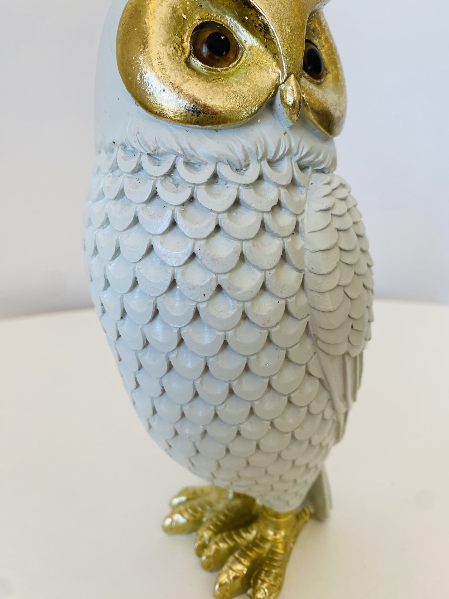 Estatueta de coruja branca e dourada com padrões de penas e olhos castanhos