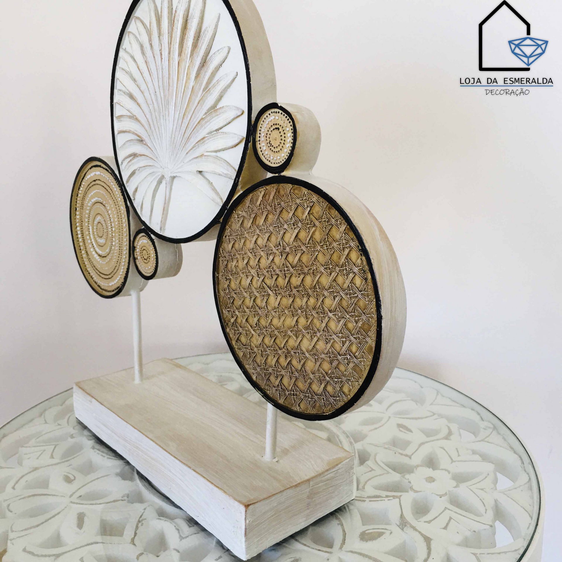 Escultura decorativa circular em madeira e palha sobre mesa de vidro, com logo Loja da Esmeralda Decoração ao fundo