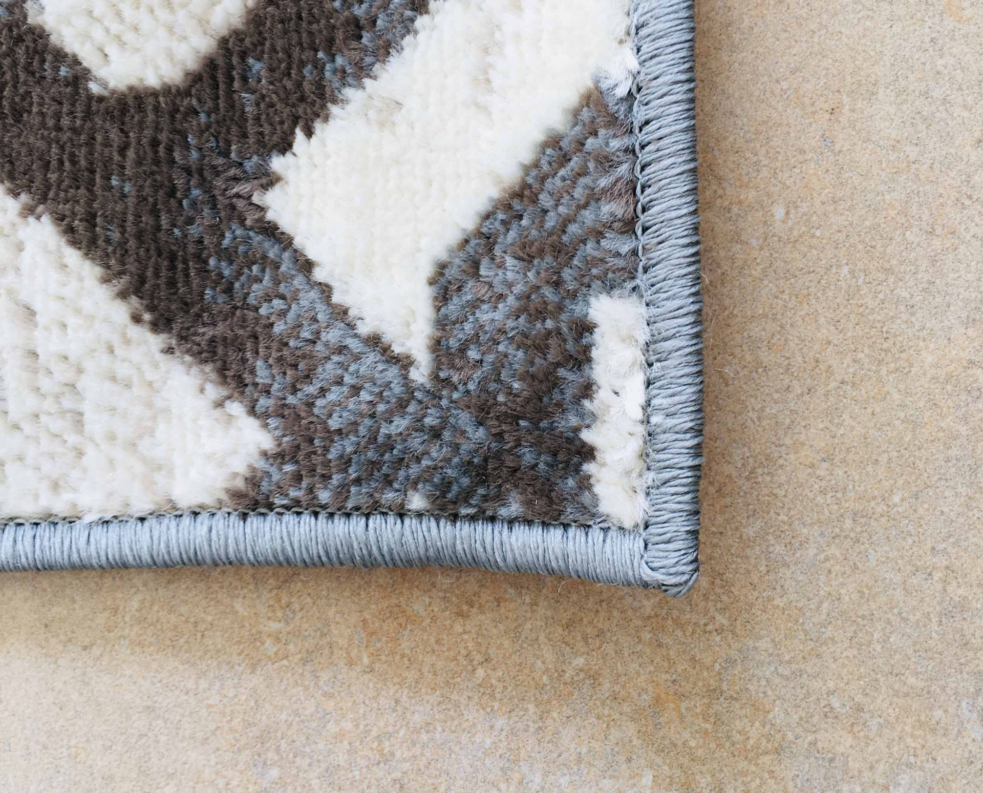 Canto de tapete cinza e branco com borda azul claro sobre piso azul claro