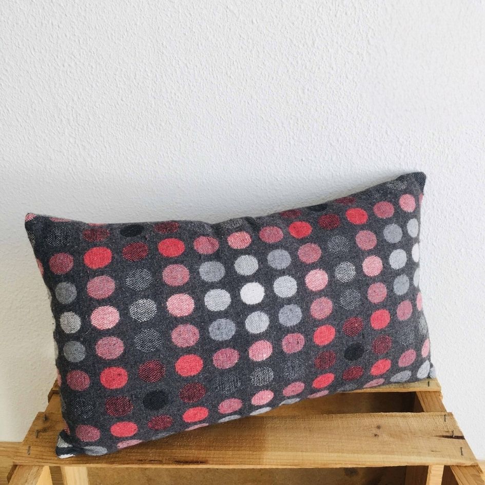 Almofada retangular com padrão de círculos coloridos sobre banco de madeira