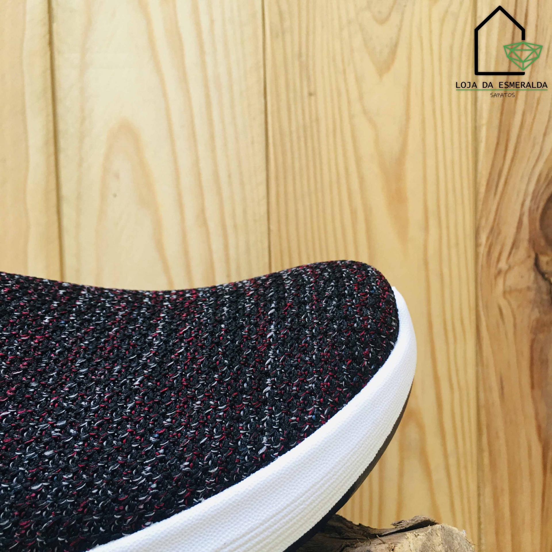 Tênis preto texturizado com sola branca sobre fundo de madeira