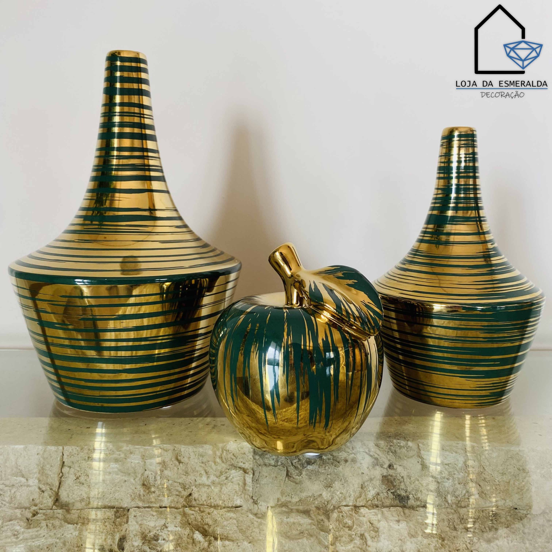 Três vasos decorativos dourados e verdes em cerâmica sobre superfície de pedra clara