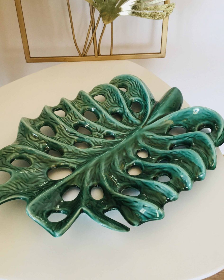 Prato decorativo de cerâmica verde em forma de folha com buracos sobre mesa branca