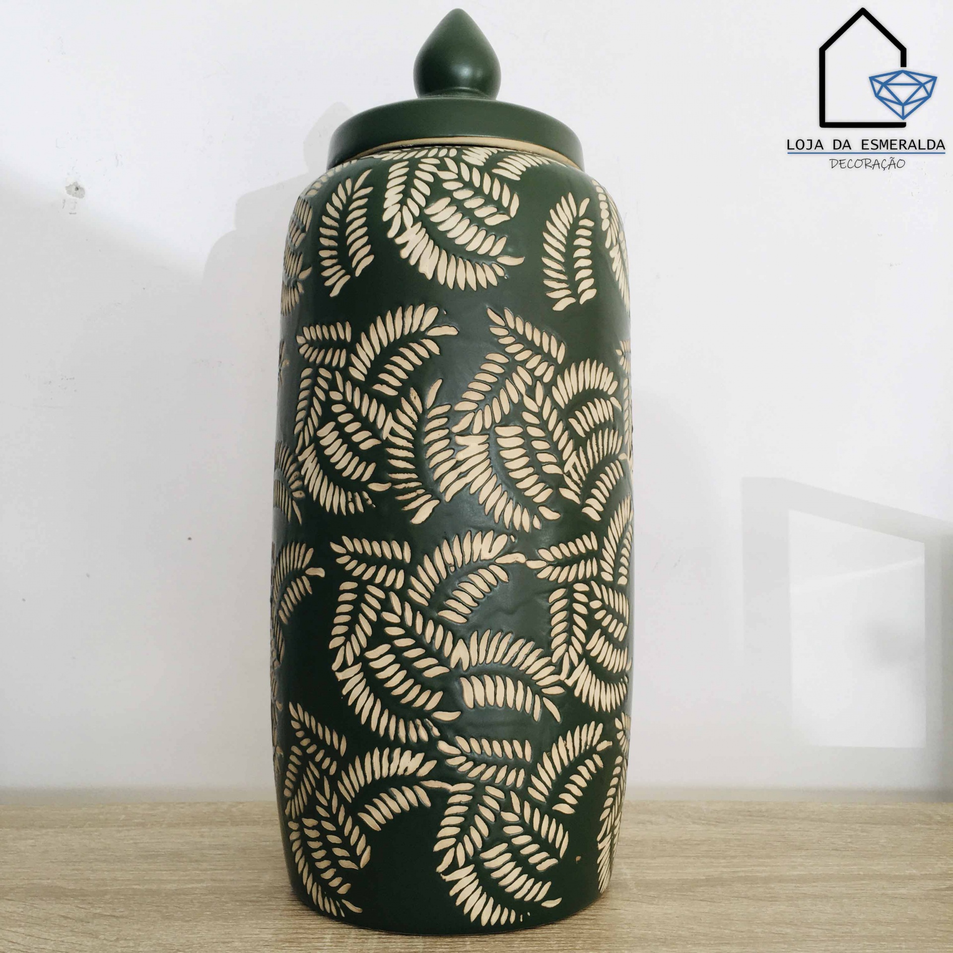 Pote decorativo em cerâmica verde com padrão de folhas bege e tampa, em superfície de madeira clara.