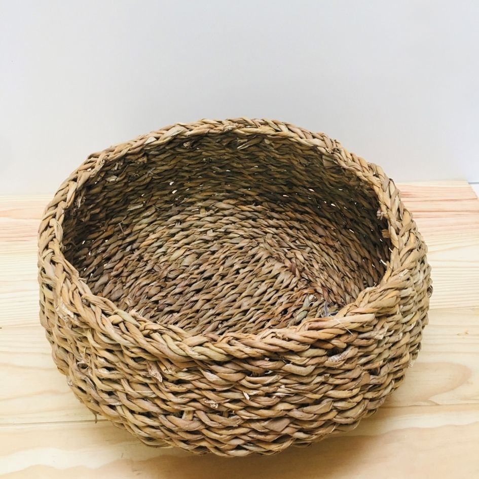 Cesto redondo de palha trançada em tons castanhos sobre madeira clara