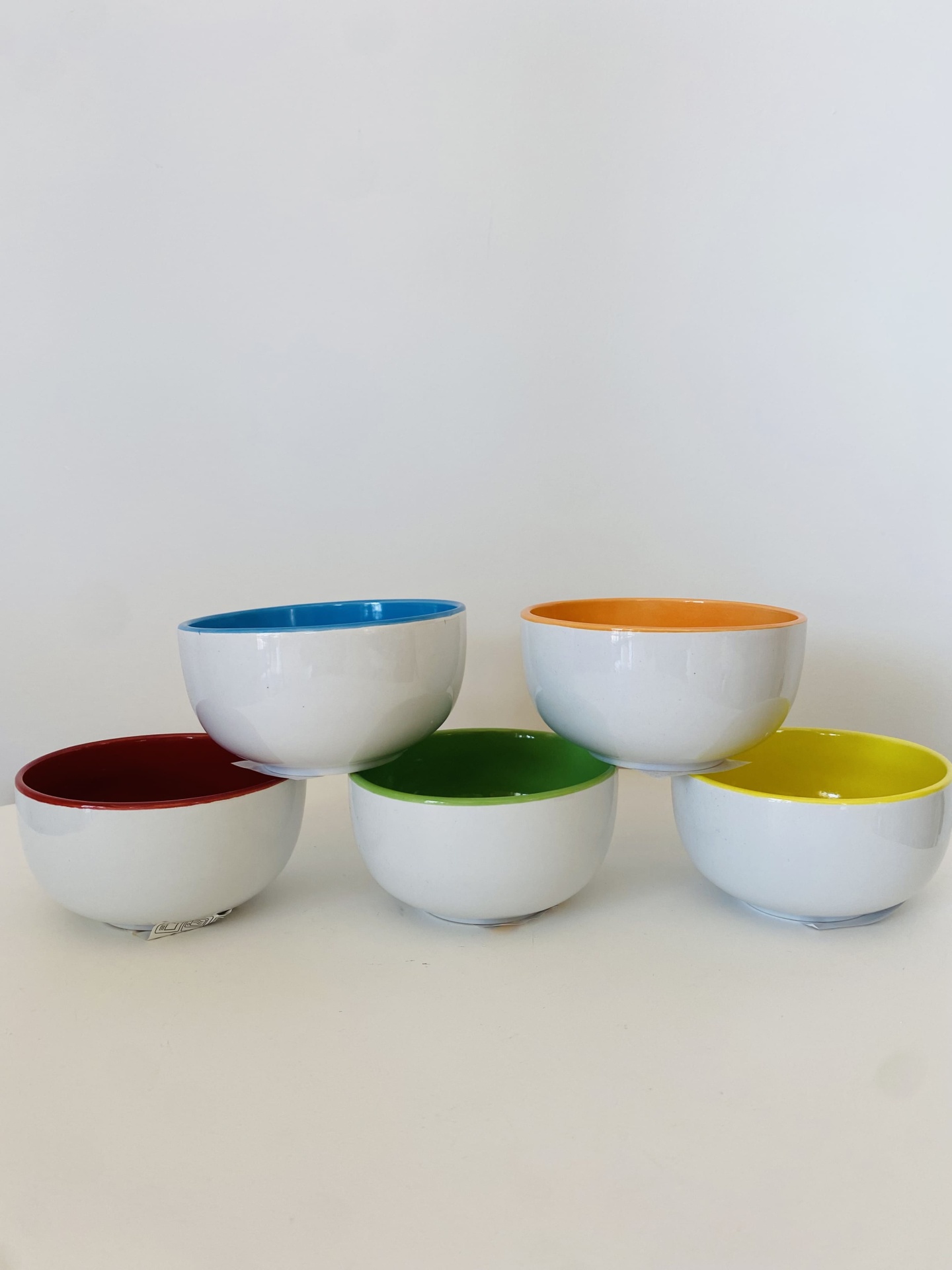 Cinco tacinhas brancas com interiores coloridos em azul, laranja, vermelho, verde e amarelo