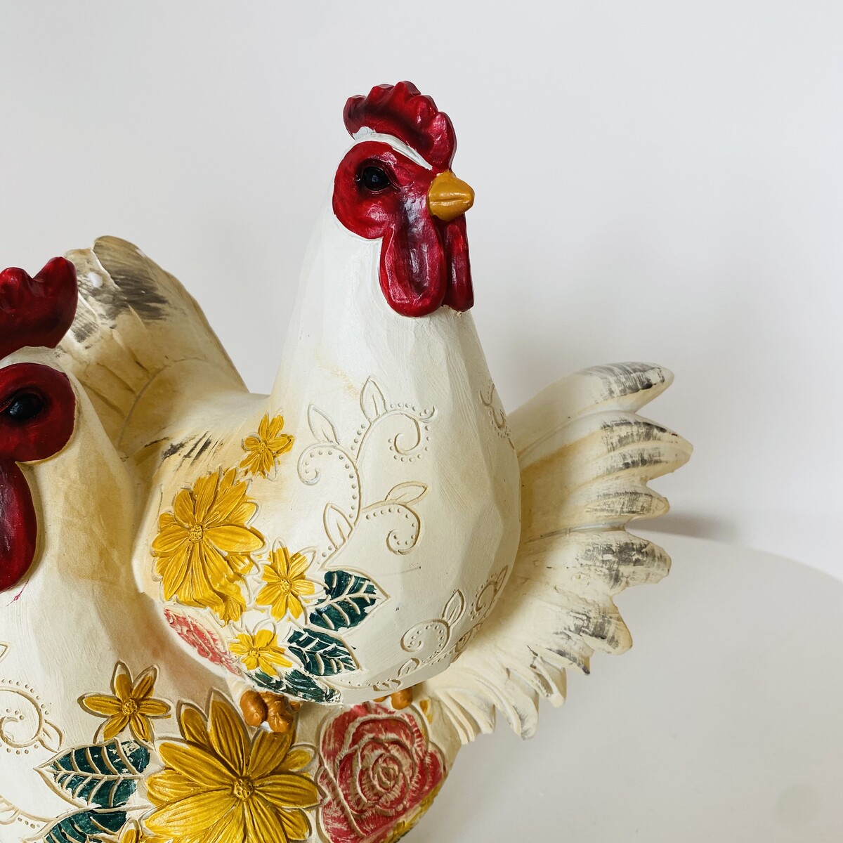 Escultura de dois galos em madeira pintada com detalhes florais coloridos