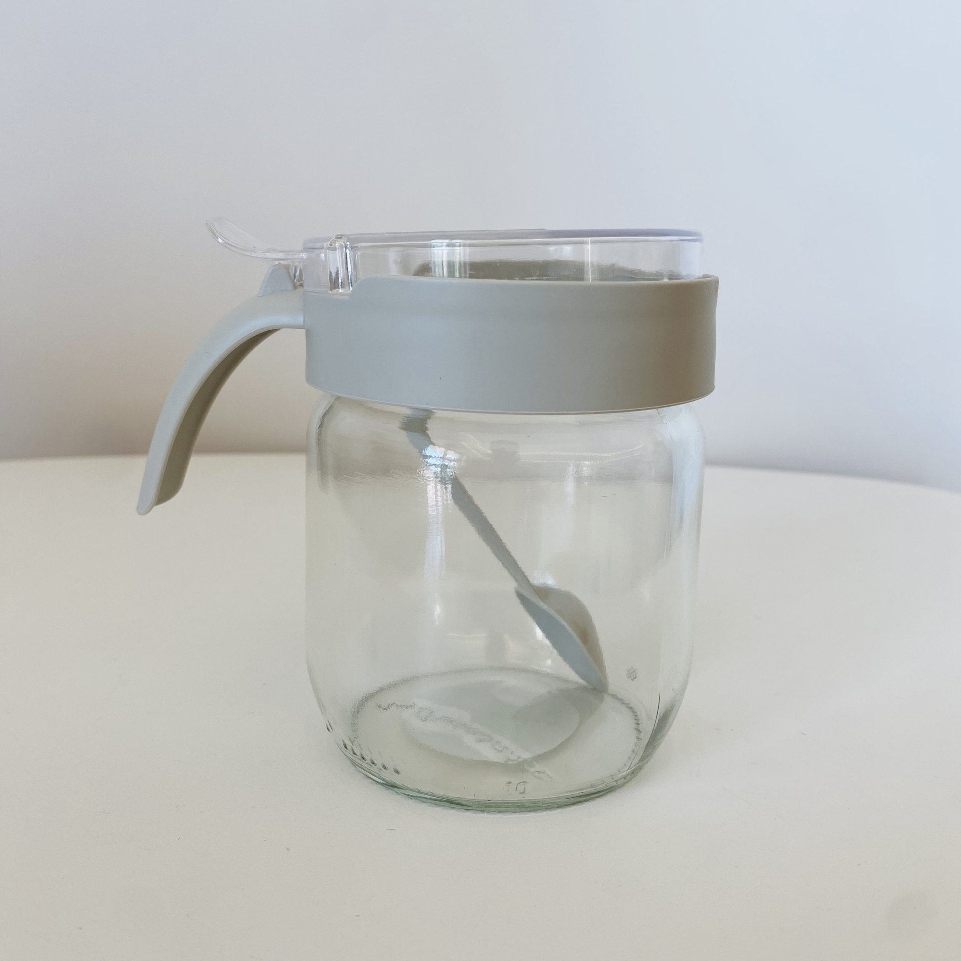 Frasco de vidro transparente com tampa cinza e colher integrada.