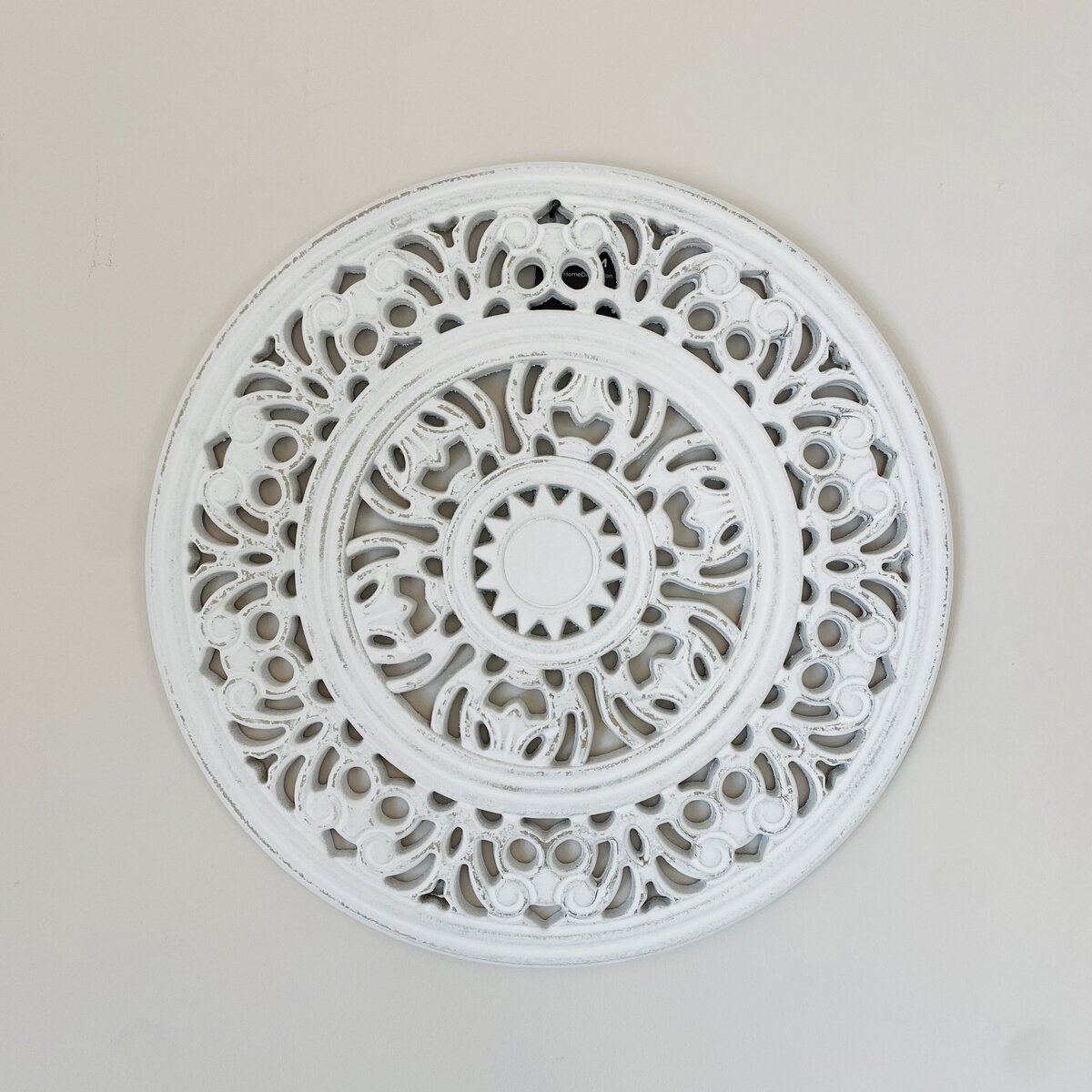 Painel decorativo circular branco com padrão recortado sobre parede cinza claro