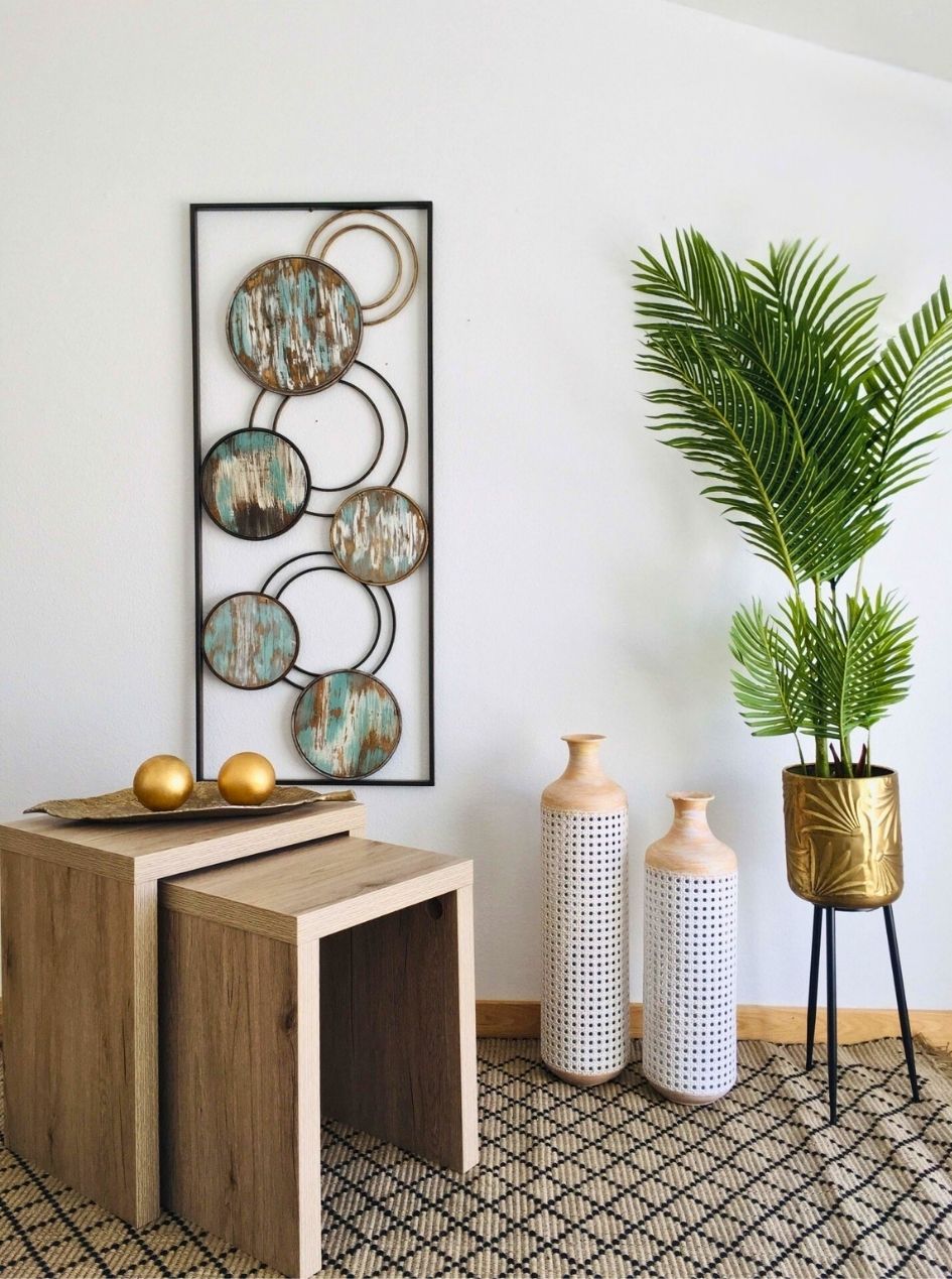 Decoração interior com mesas de madeira, vasos decorativos, planta verde em vaso dourado e quadro de círculos em madeira