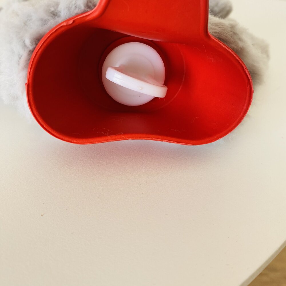 Rolo de fita adesiva vermelha com carretel branco numa superfície branca com textura cinza clara ao redor.