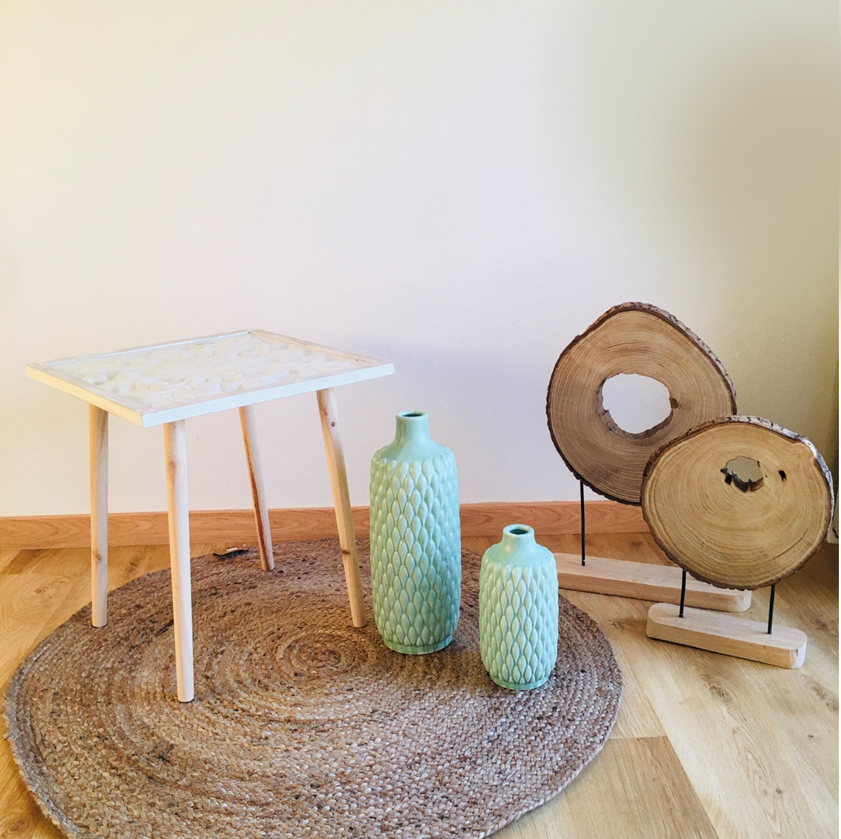 Mesa branca com vasos cerâmicos verdes e decoração de madeira sobre tapete redondo