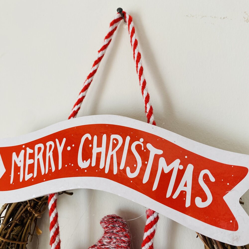 Placa decorativa vermelha e branca com a frase MERRY CHRISTMAS pendurada na parede