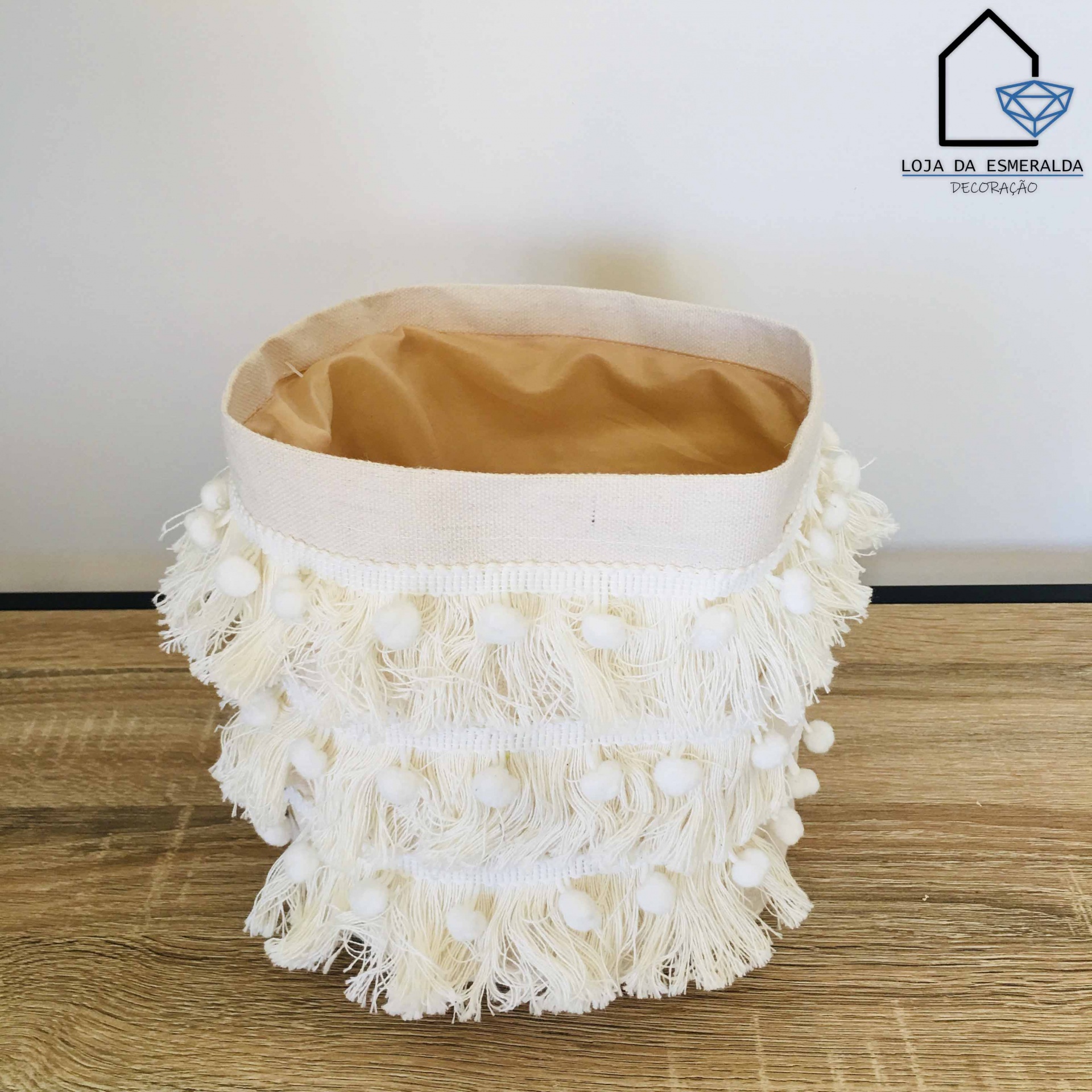 Cesto decorativo branco com franjas e pompons numa superfície de madeira