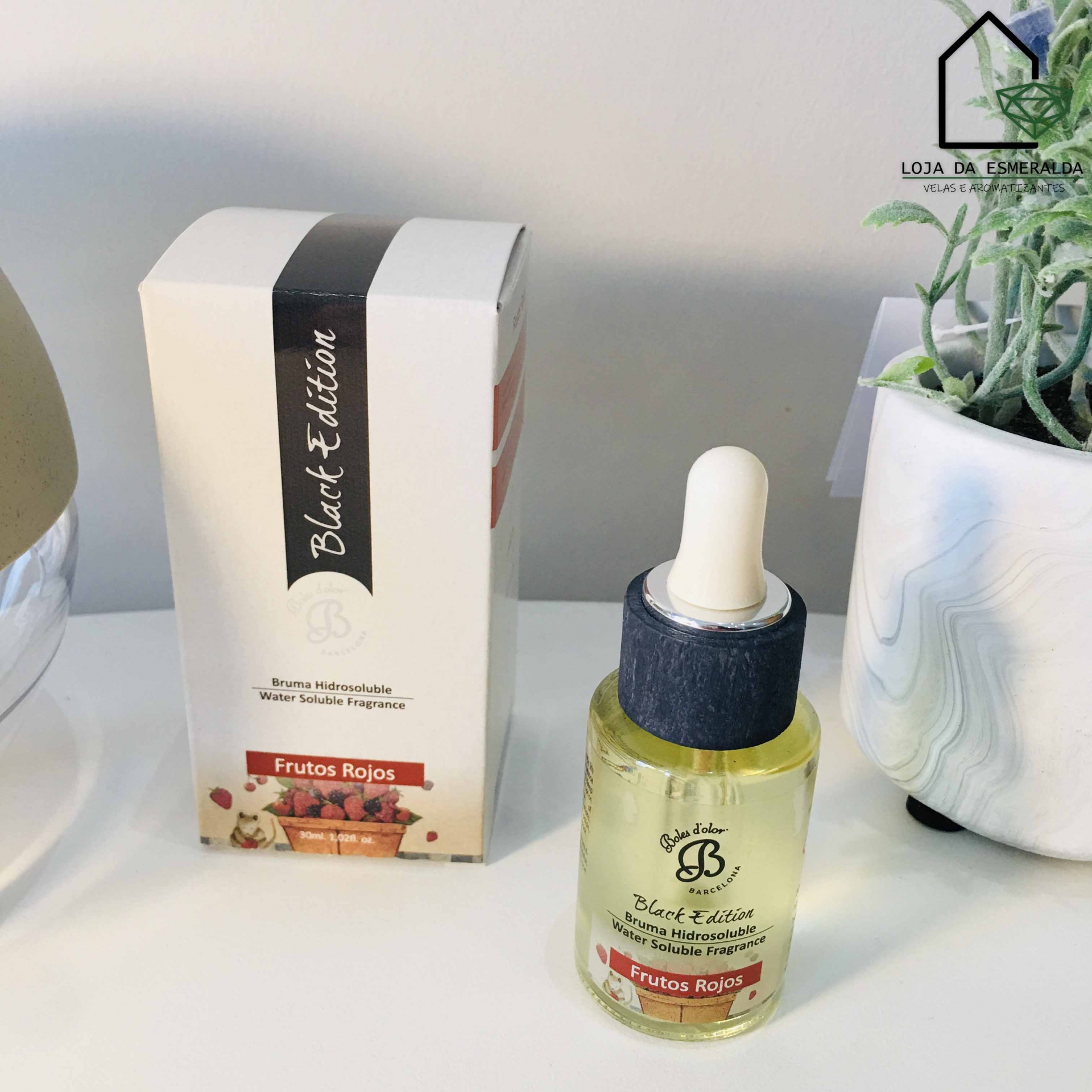 Frasco com conta-gotas de óleo ou sérum e caixa da linha Black Edition Frutos Rojos num fundo branco ao lado de planta