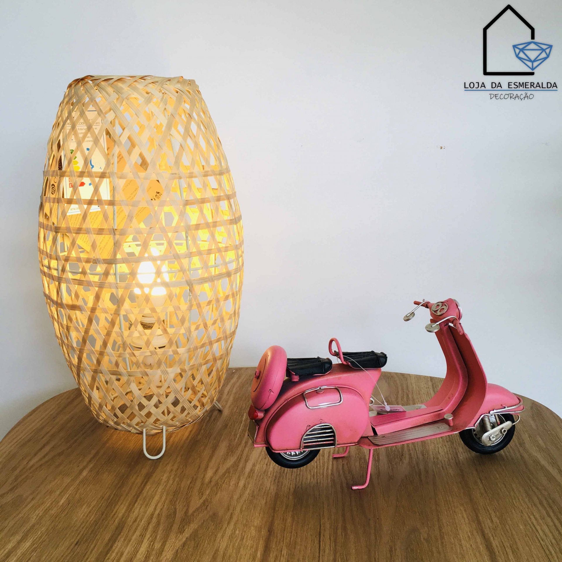 Abajur oval trançado de verga e mota miniatura rosa sobre mesa de madeira